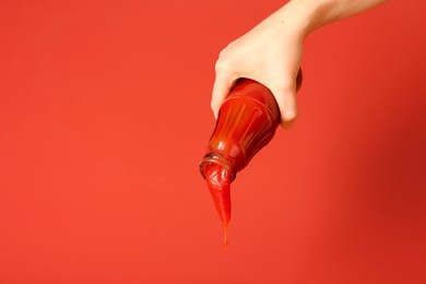 Photo of Woman pouring ketchup out of bottle on red background, closeup. Space for text