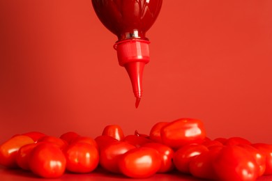 Photo of Squeezing ketchup from bottle over tomatoes on red background, closeup