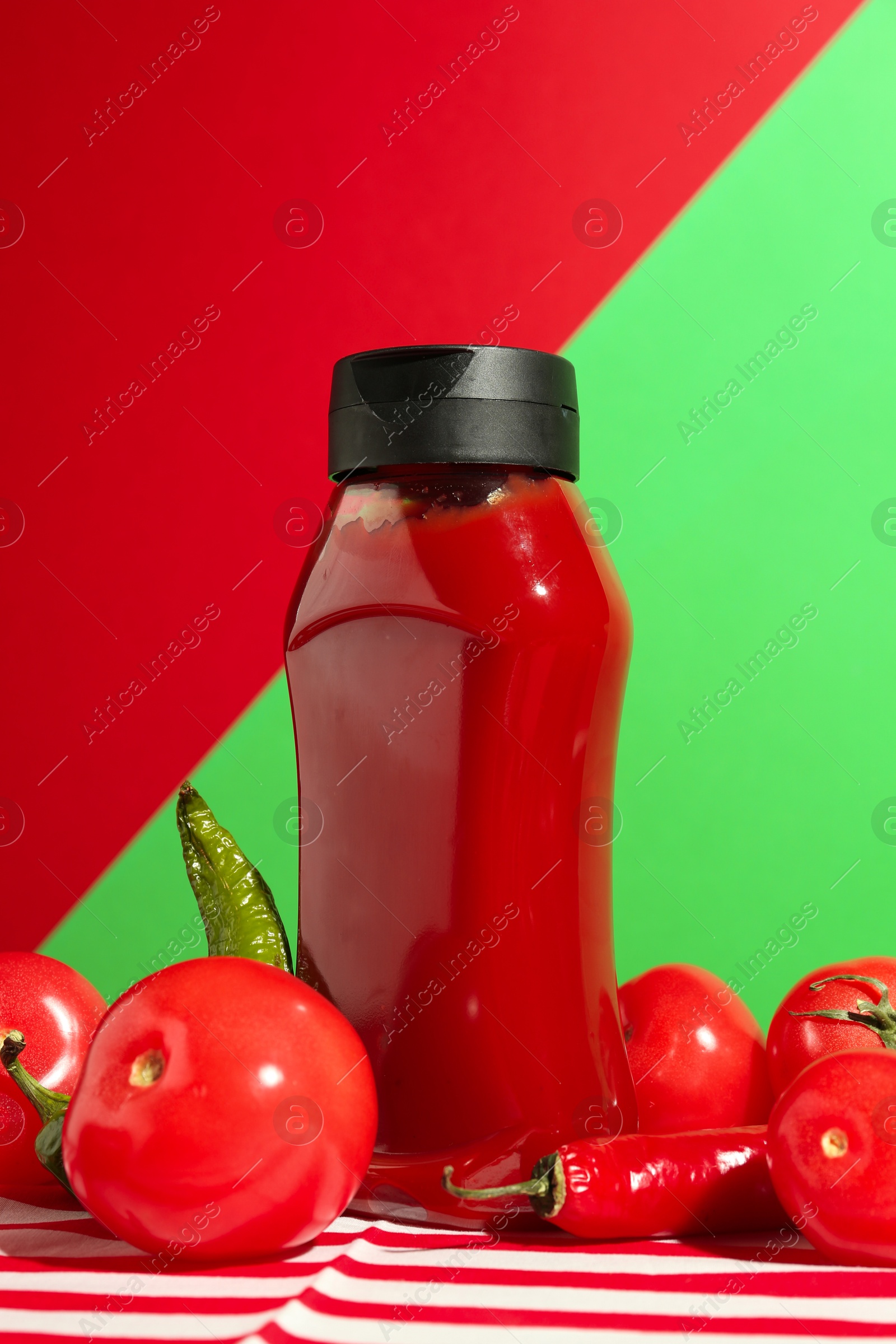 Photo of Bottle of ketchup, tomatoes and chili peppers on color background