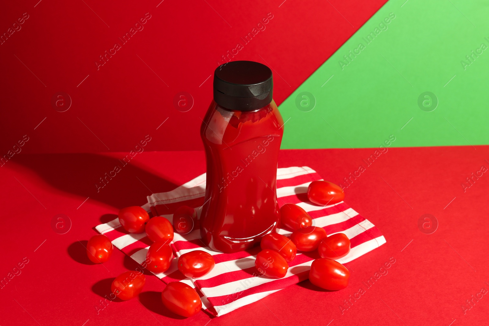 Photo of Bottle of ketchup and tomatoes on color background