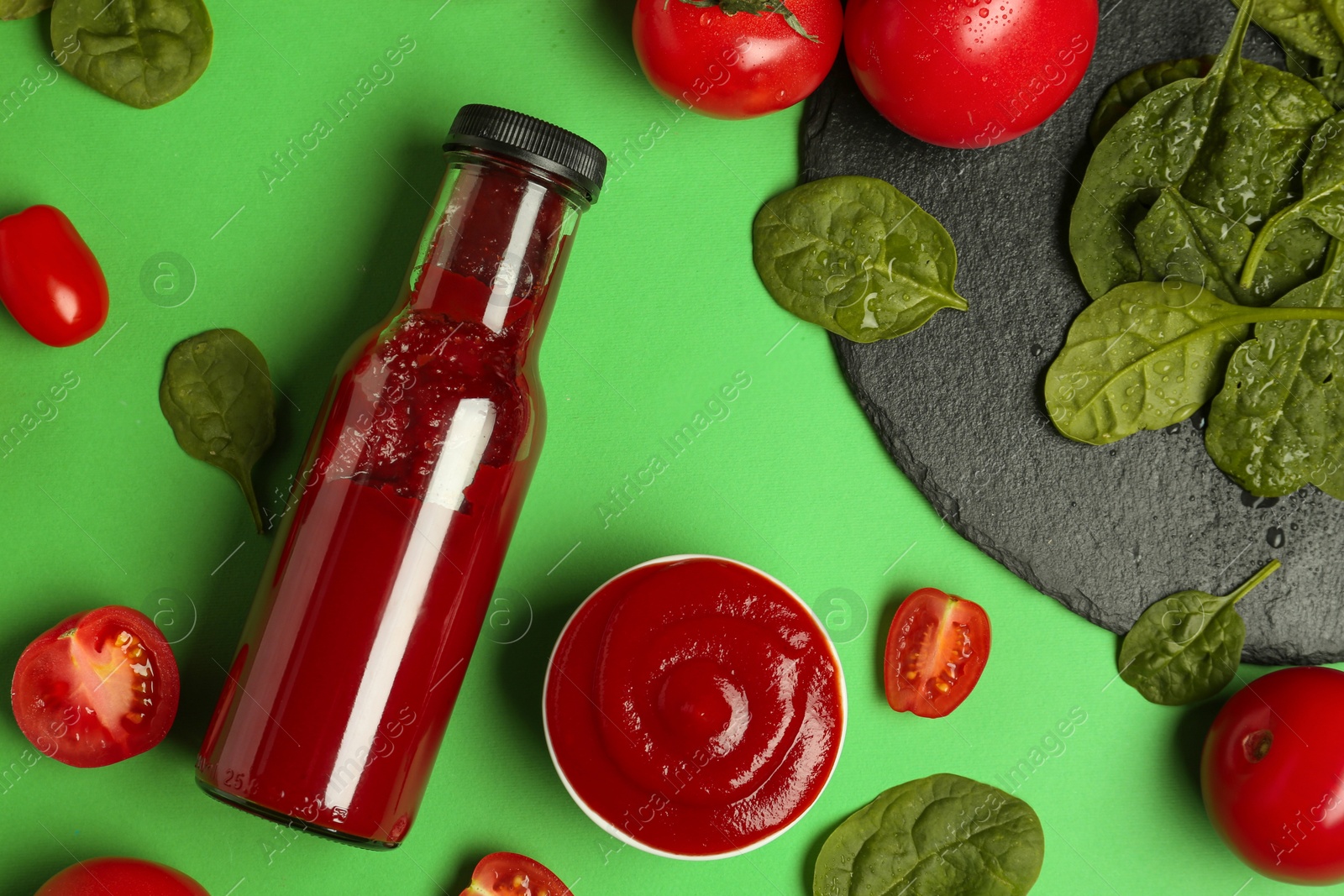 Photo of Ketchup, tomatoes and spinach on green background, flat lay