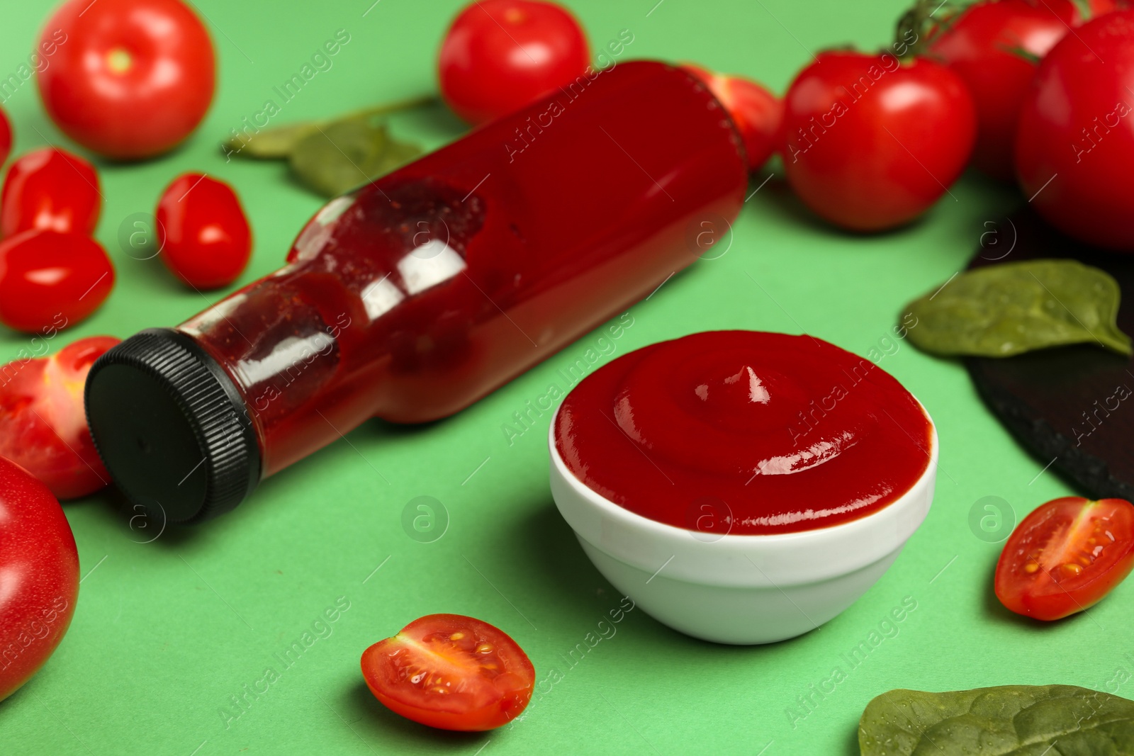 Photo of Ketchup, tomatoes and spinach on green background, closeup