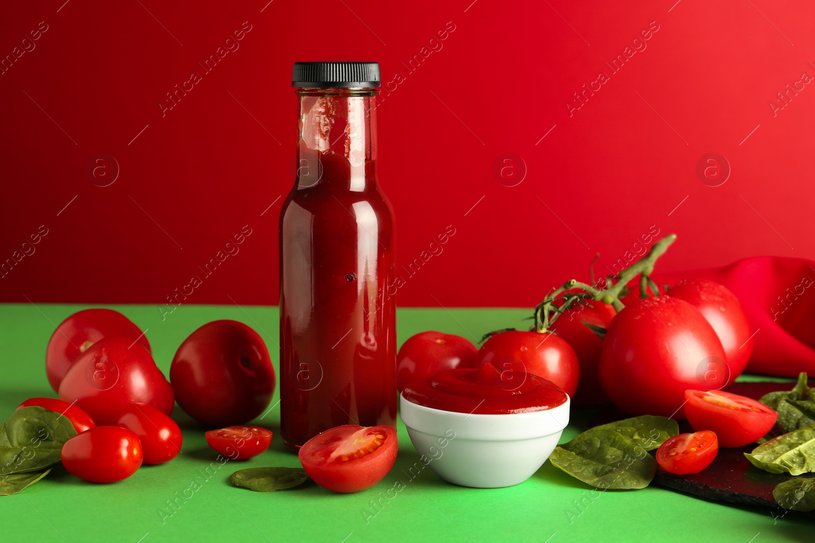 Photo of Ketchup, tomatoes and spinach on color background