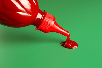 Photo of Squeezing ketchup from bottle on green background, closeup