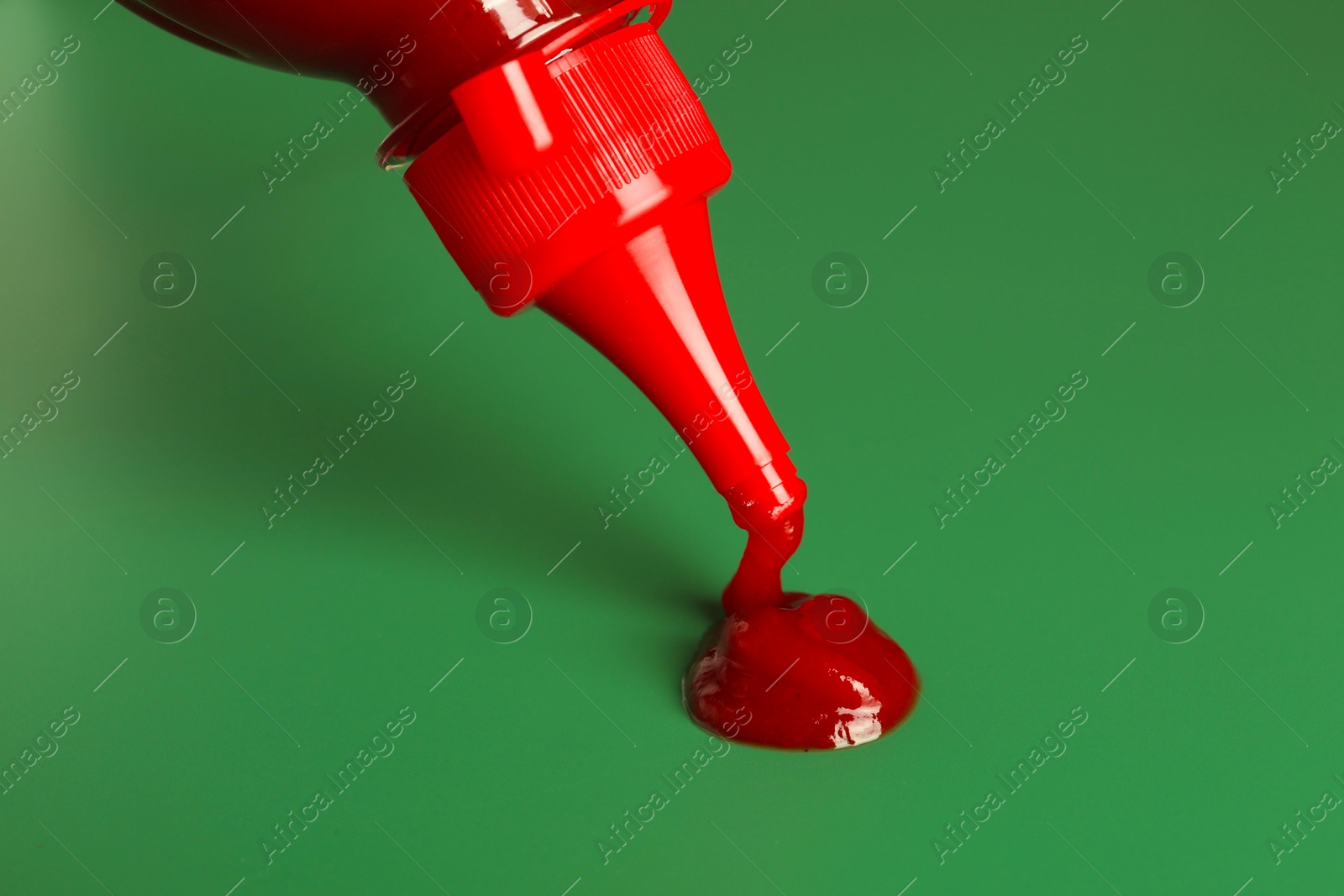 Photo of Squeezing ketchup from bottle on green background, closeup