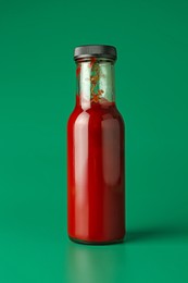 Photo of Tasty ketchup in bottle on green background