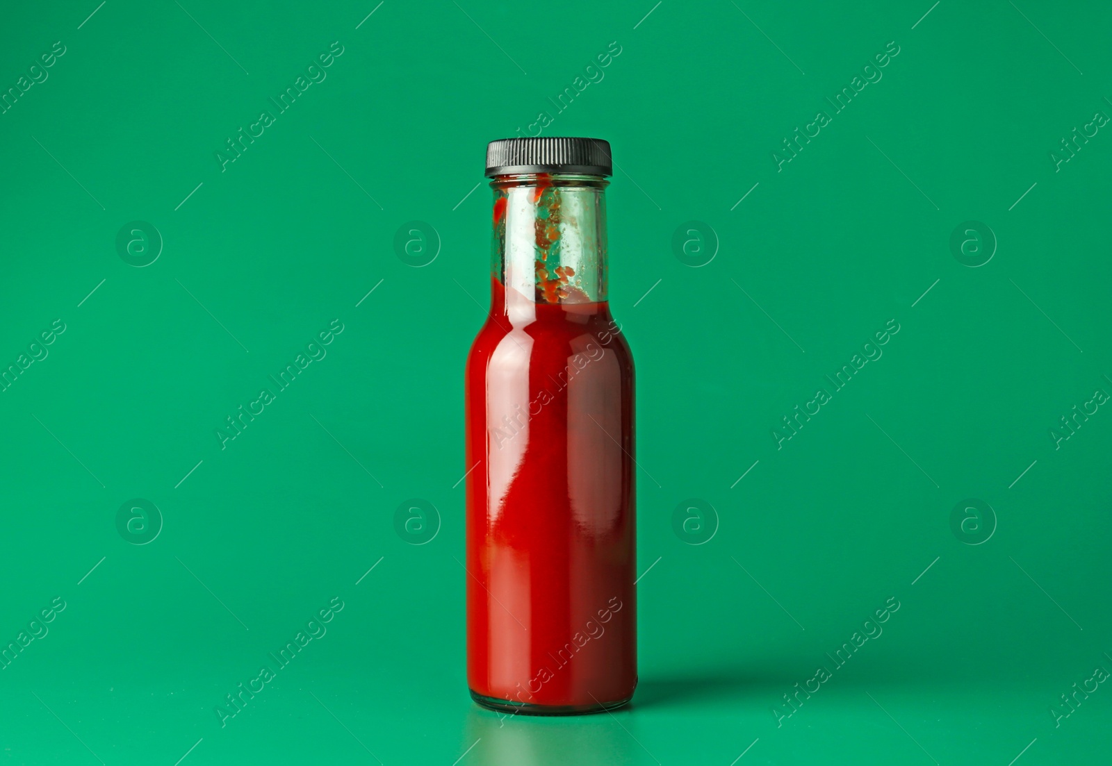 Photo of Tasty ketchup in bottle on green background