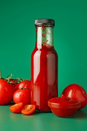 Photo of Ketchup in bottle and fresh tomatoes on green background