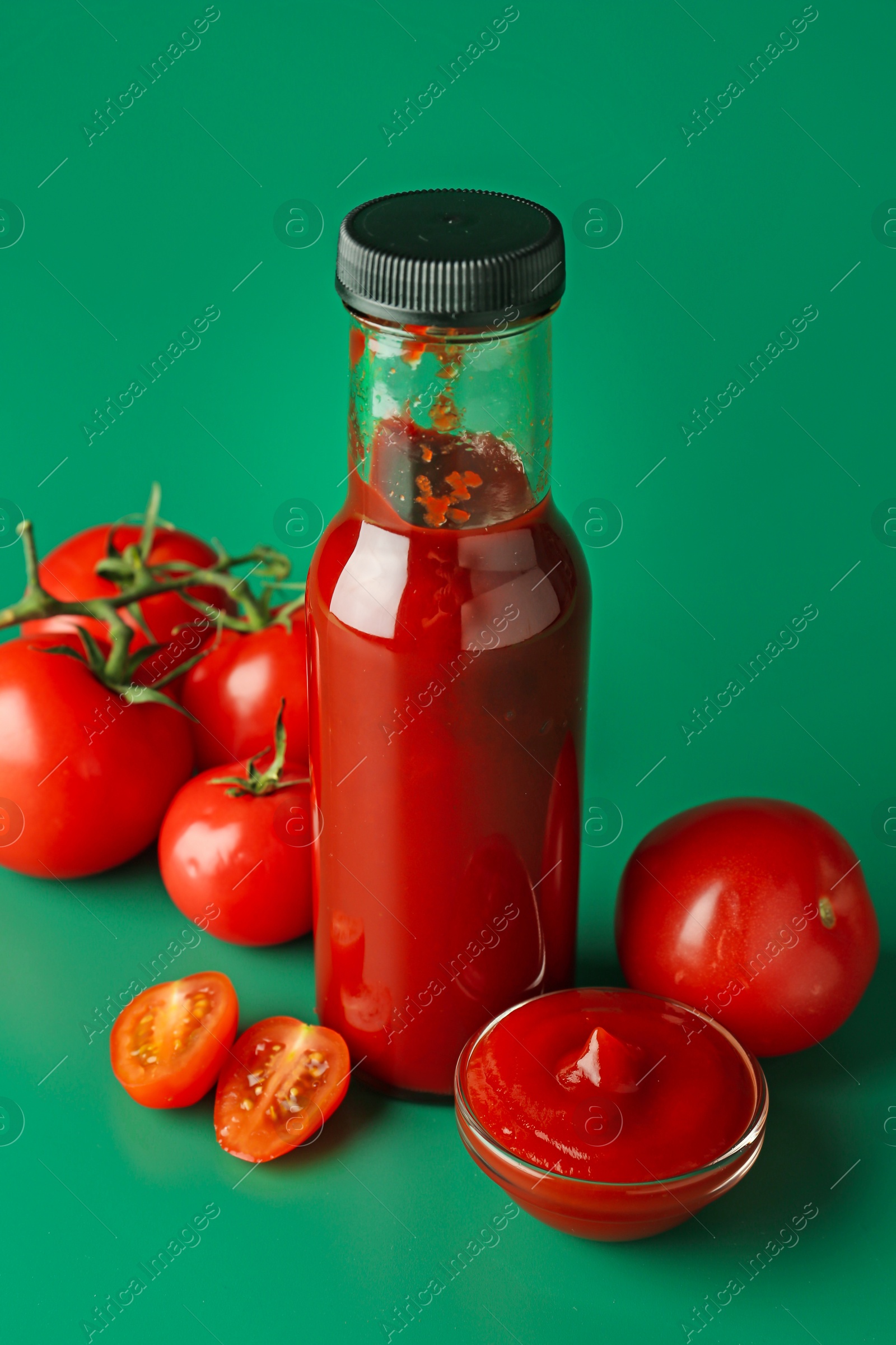 Photo of Ketchup in bottle and fresh tomatoes on green background