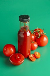 Photo of Ketchup in bottle and fresh tomatoes on green background