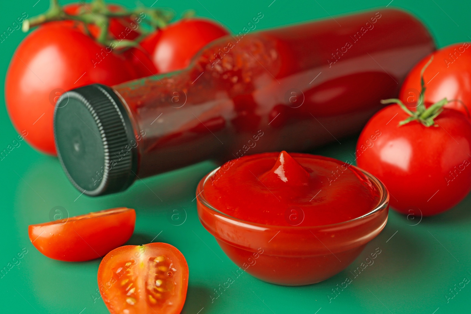 Photo of Tasty ketchup and fresh tomatoes on green background, closeup