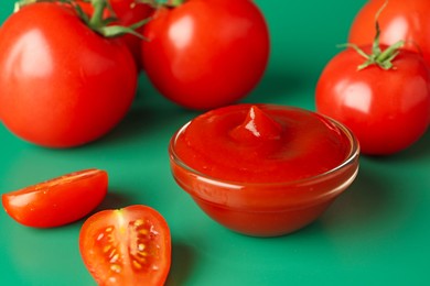 Photo of Tasty ketchup and fresh tomatoes on green background, closeup