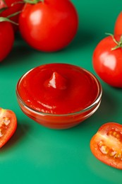 Photo of Tasty ketchup and fresh tomatoes on green background, closeup