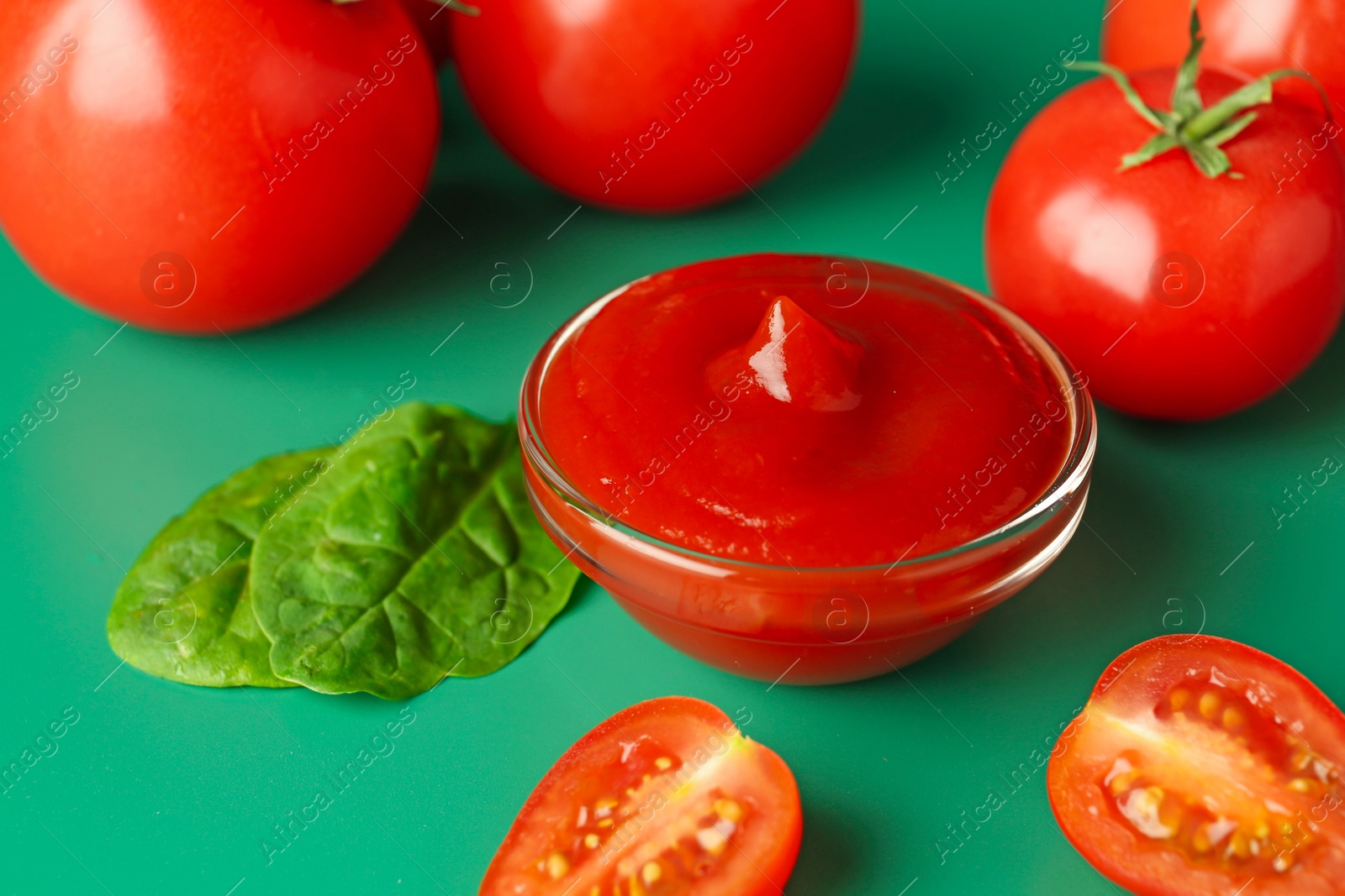 Photo of Tasty ketchup and fresh tomatoes on green background, closeup