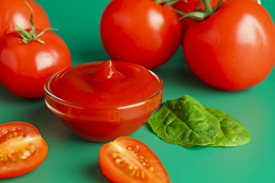 Photo of Tasty ketchup and fresh tomatoes on green background, closeup