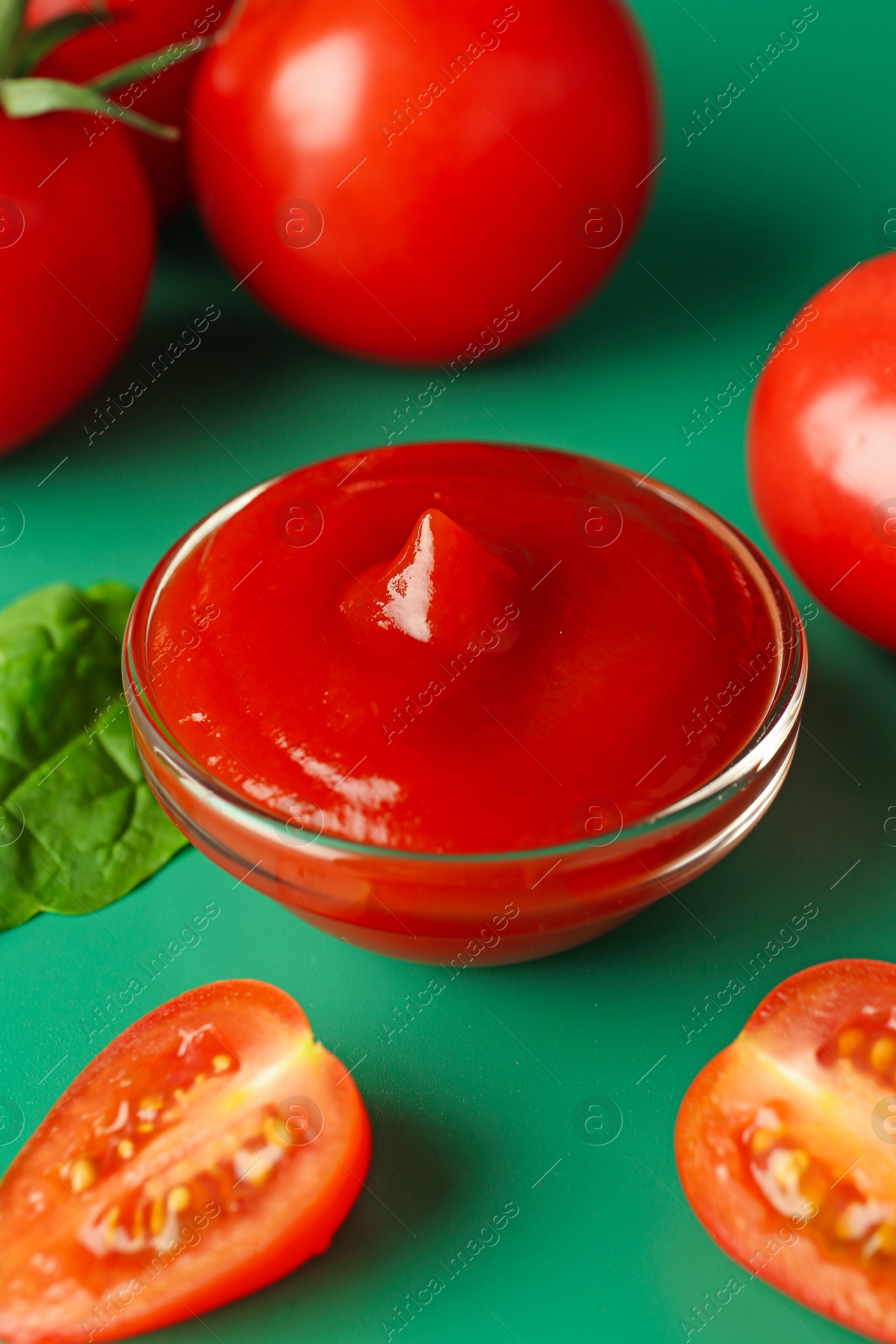 Photo of Tasty ketchup and fresh tomatoes on green background, closeup