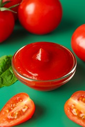 Photo of Tasty ketchup and fresh tomatoes on green background, closeup