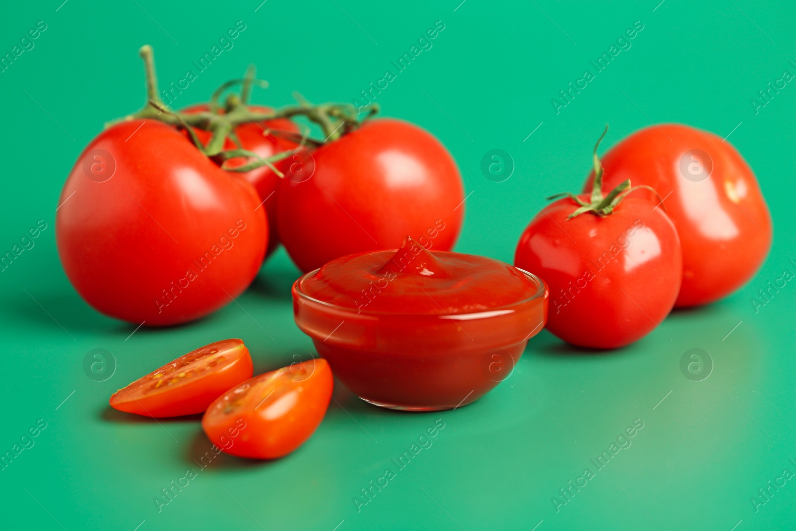 Photo of Tasty ketchup and fresh tomatoes on green background