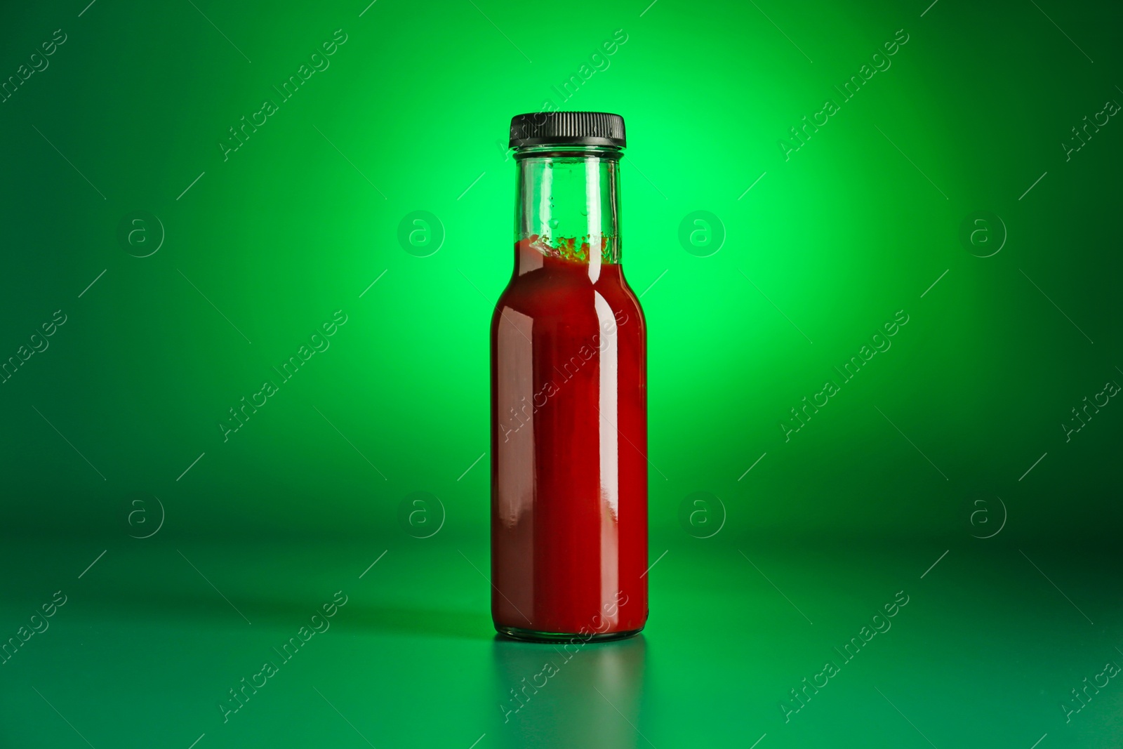 Photo of Tasty ketchup in bottle on green background