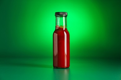 Photo of Tasty ketchup in bottle on green background