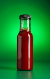 Photo of Tasty ketchup in bottle on green background