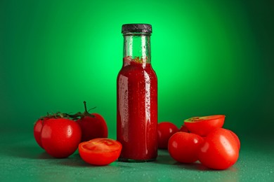 Photo of Ketchup in bottle and fresh tomatoes on green background