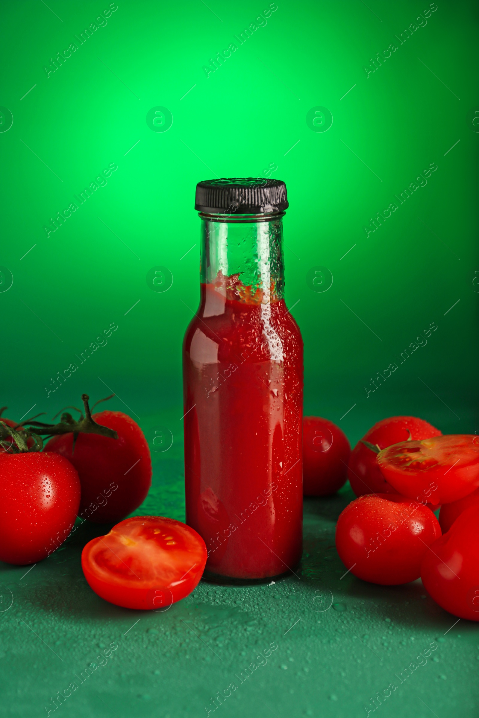 Photo of Ketchup in bottle and fresh tomatoes on green background