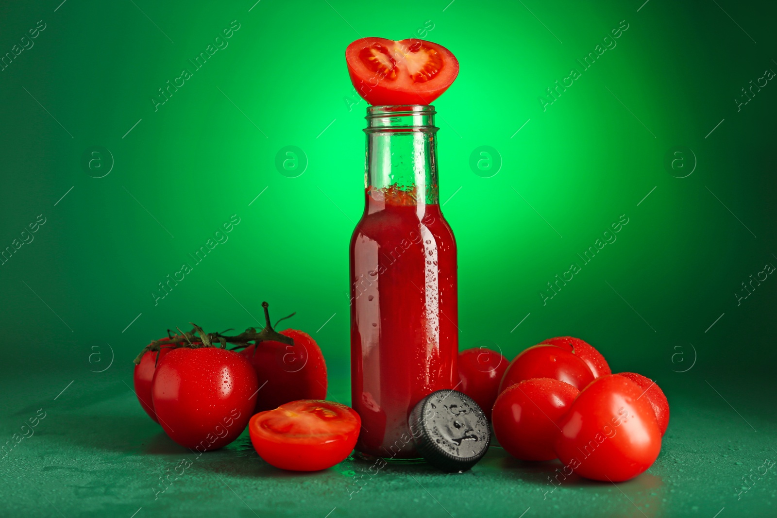 Photo of Ketchup in bottle and fresh tomatoes on green background