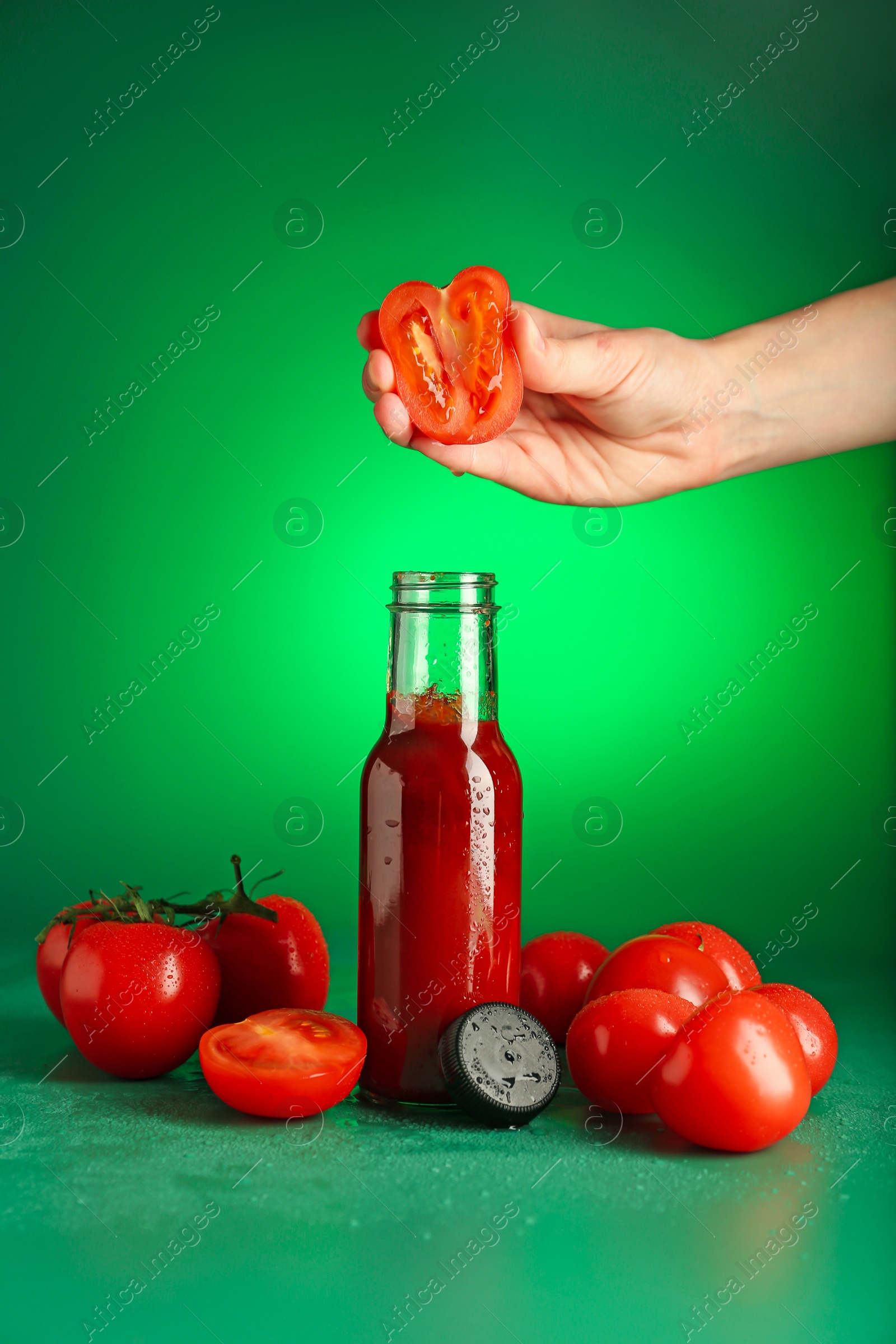 Photo of Woman squeezing tomato into bottle of ketchup on green background, closeup