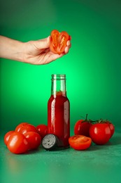 Photo of Woman squeezing tomato into bottle of ketchup on green background, closeup