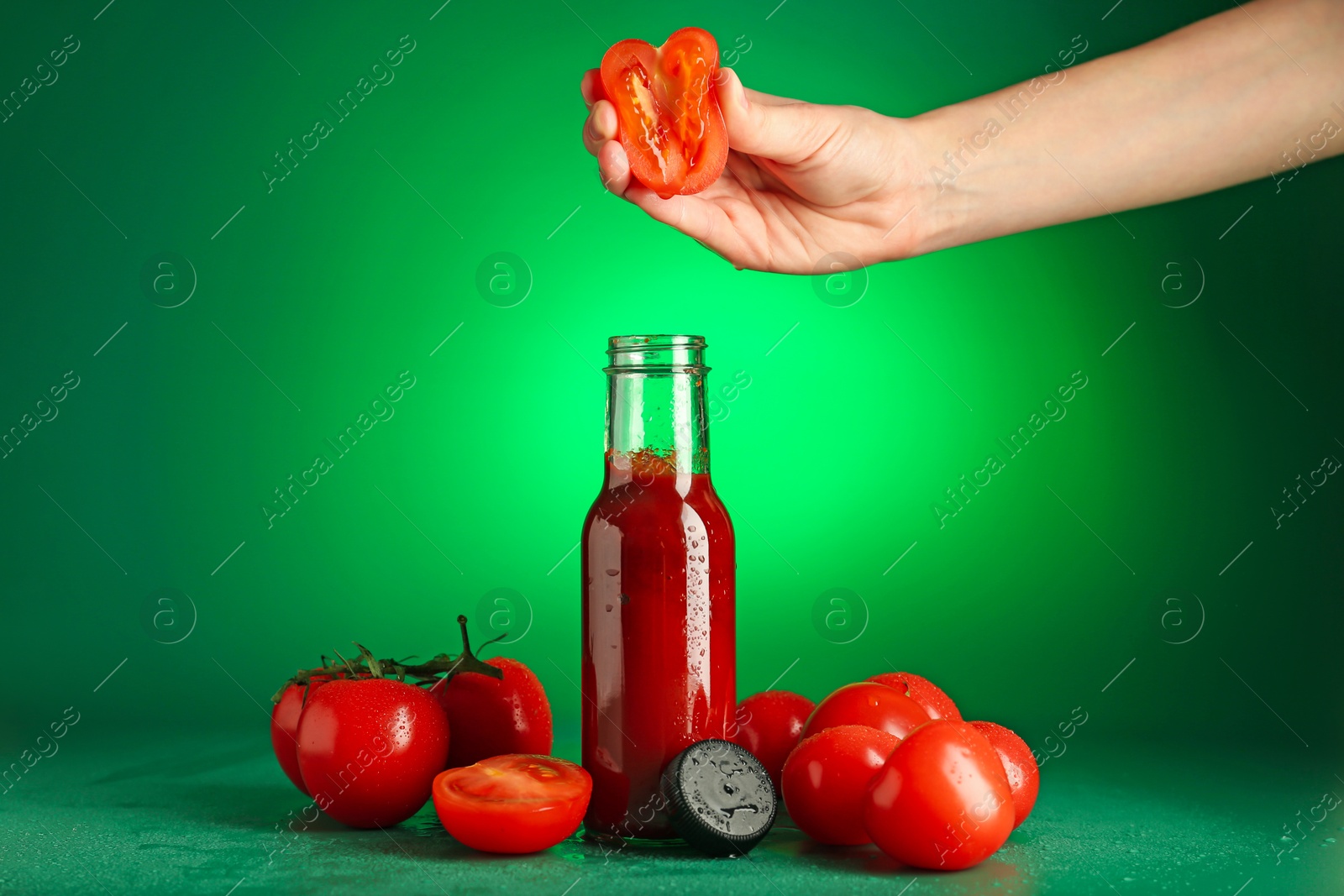 Photo of Woman squeezing tomato into bottle of ketchup on green background, closeup