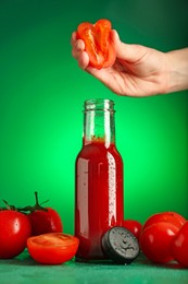 Photo of Woman squeezing tomato into bottle of ketchup on green background, closeup