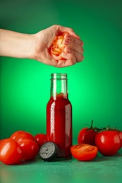 Photo of Woman squeezing tomato into bottle of ketchup on green background, closeup