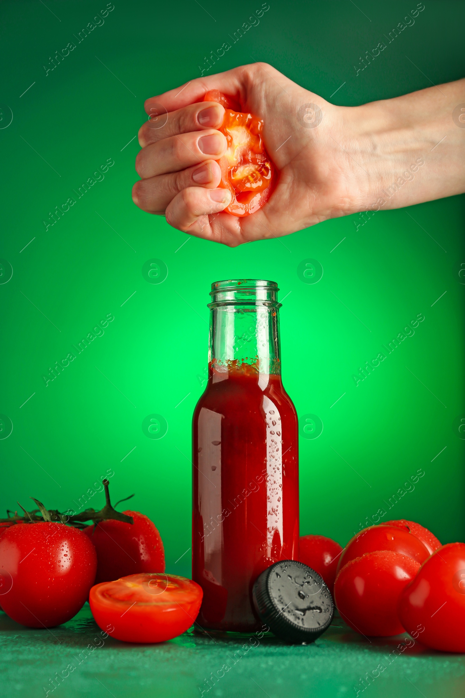 Photo of Woman squeezing tomato into bottle of ketchup on green background, closeup