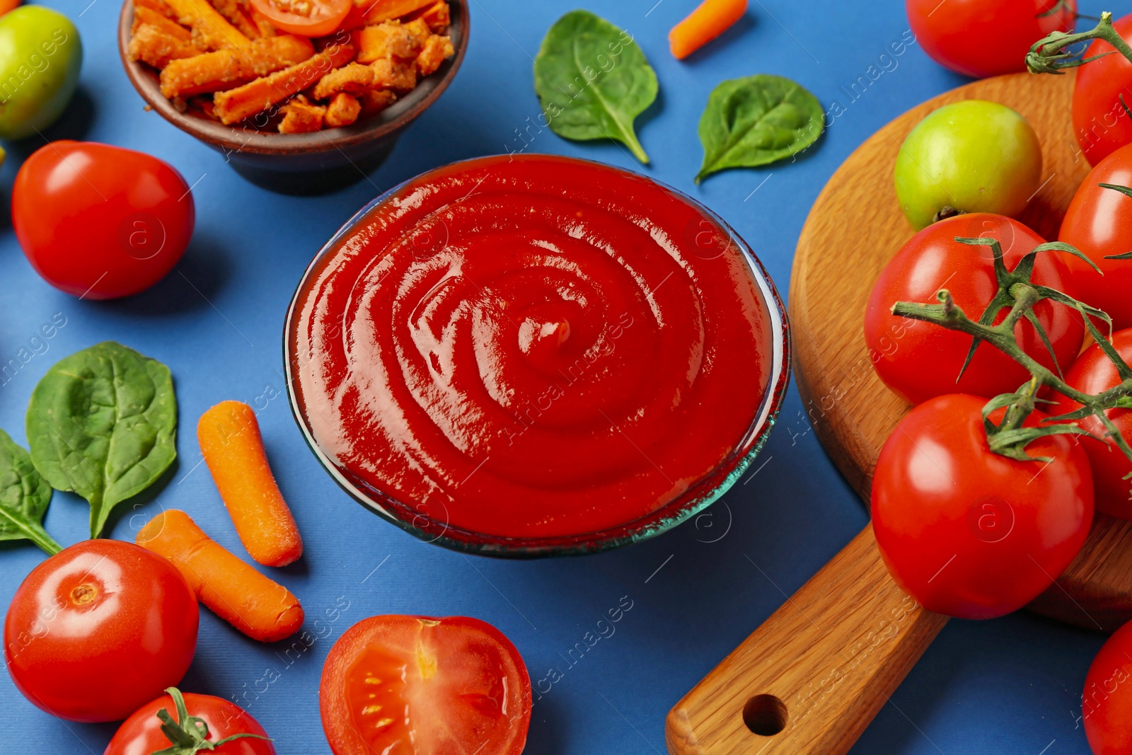 Photo of Tasty ketchup and vegetables on blue background, closeup