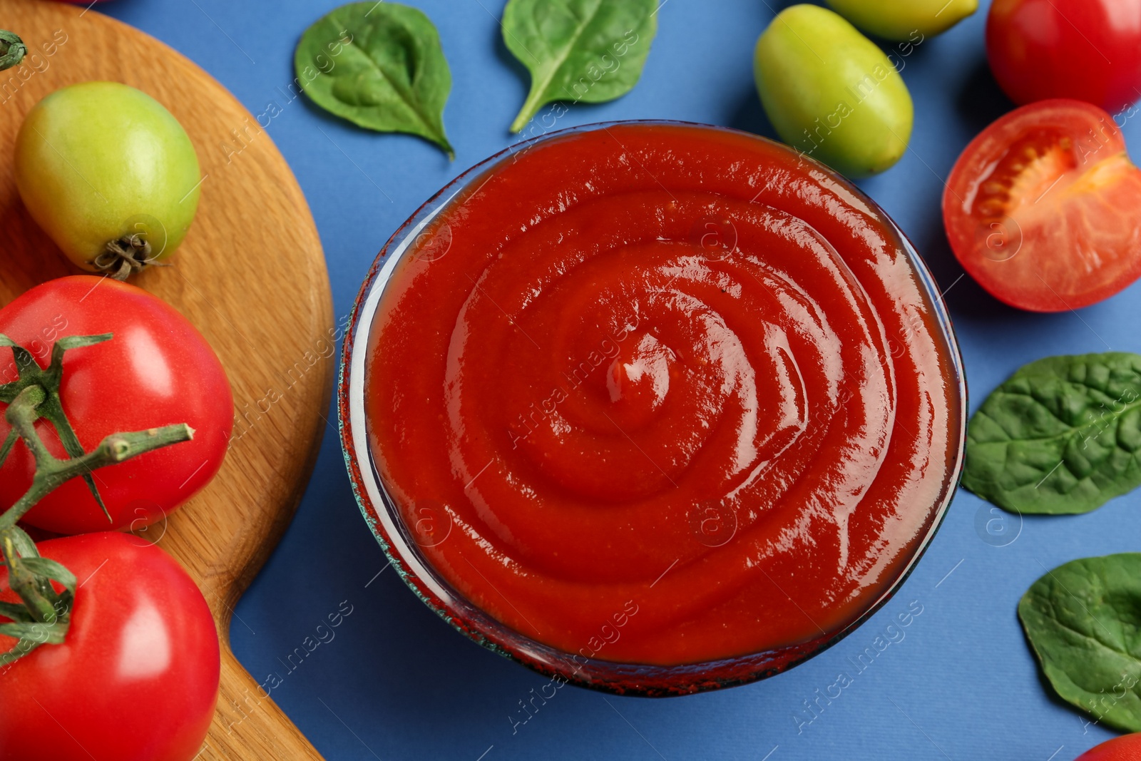 Photo of Tasty ketchup and vegetables on blue background, above view