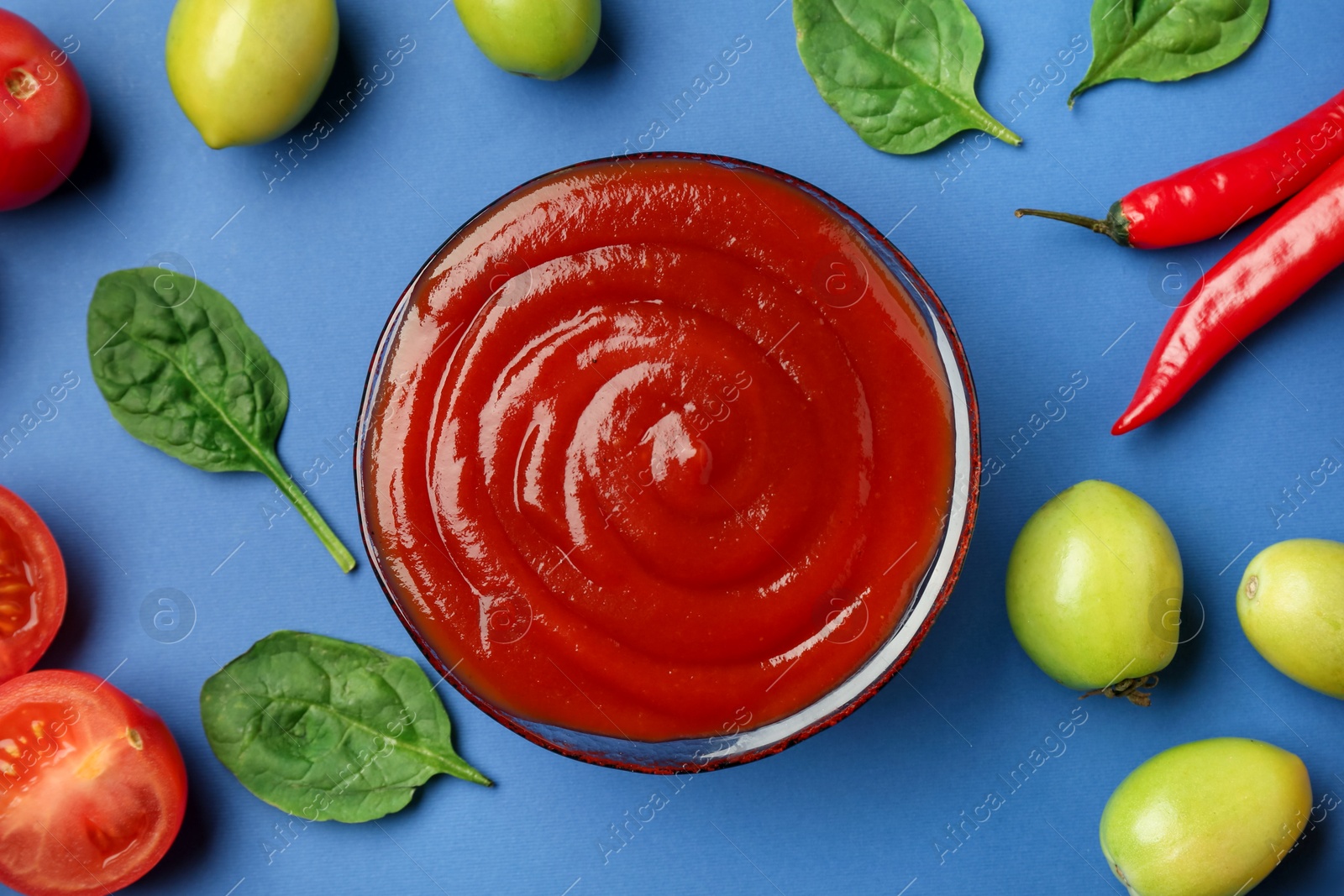 Photo of Tasty ketchup and vegetables on blue background, flat lay