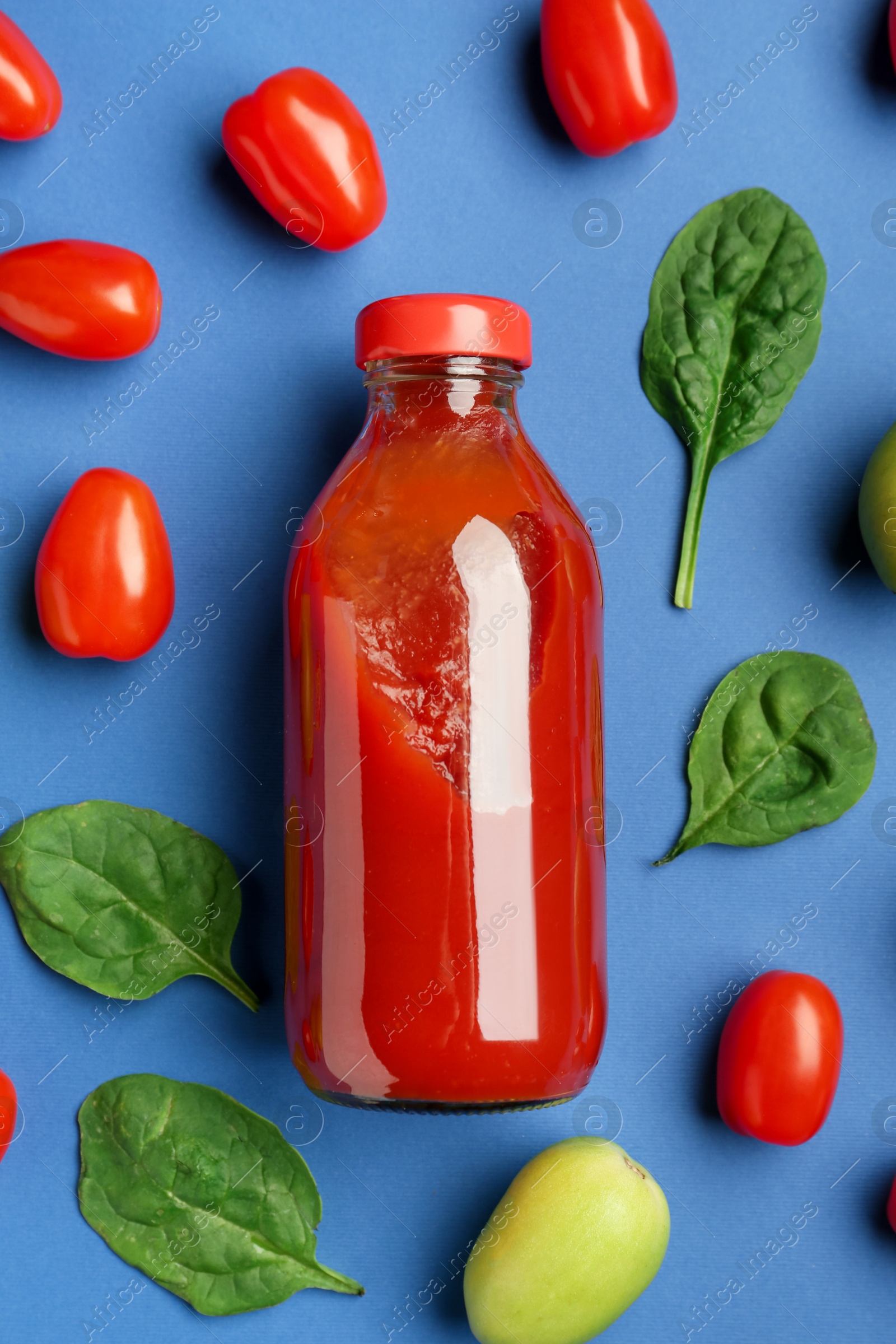 Photo of Tasty ketchup in bottle, tomatoes and basil on blue background, flat lay