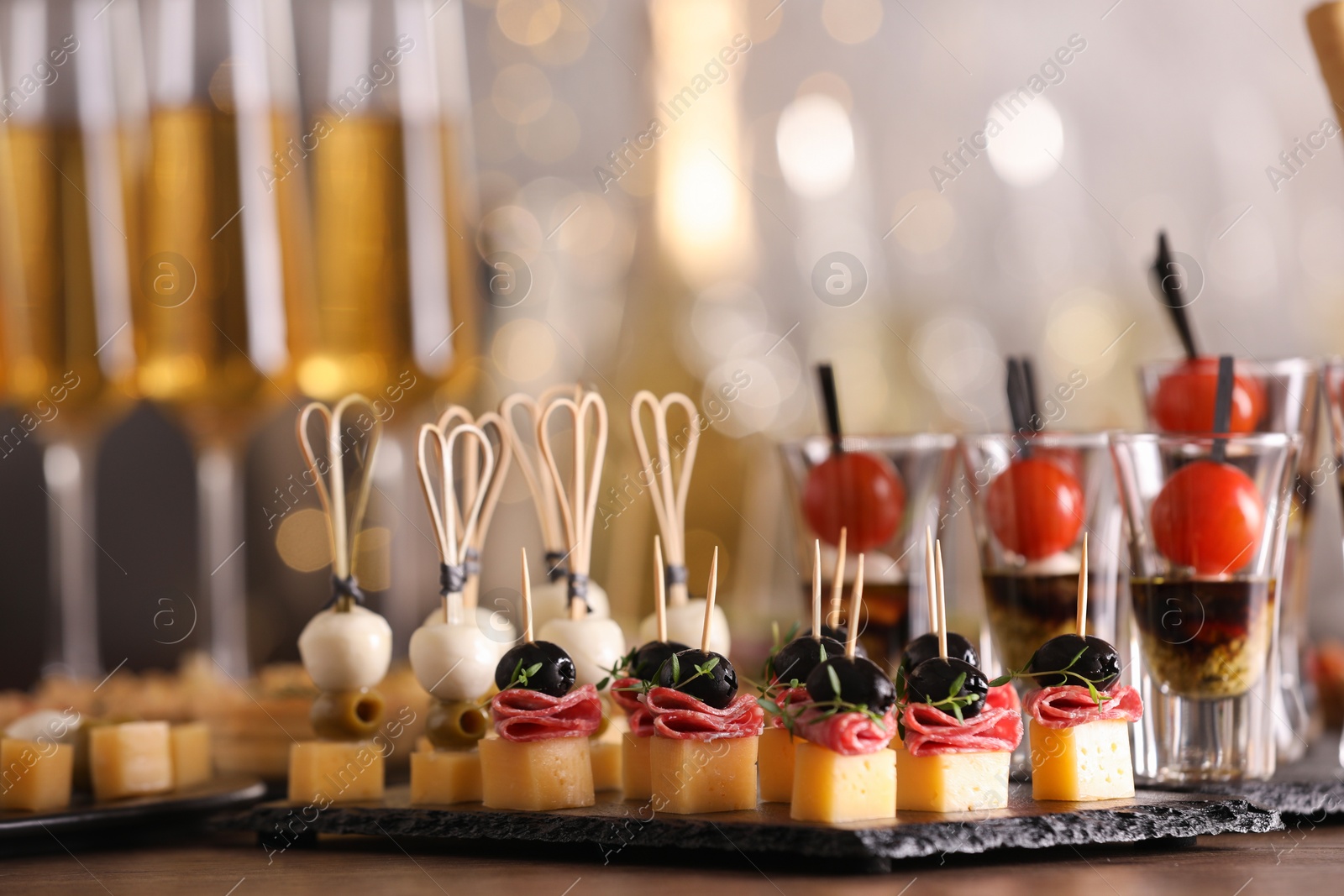 Photo of Many different tasty canapes on wooden table against blurred lights, closeup