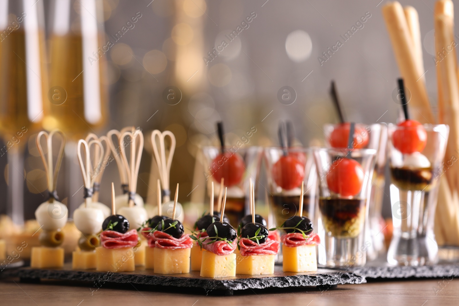 Photo of Many different tasty canapes on wooden table against blurred lights, closeup