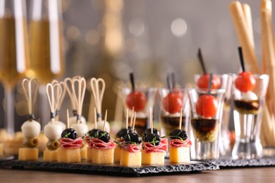 Photo of Many different tasty canapes on wooden table against blurred lights, closeup