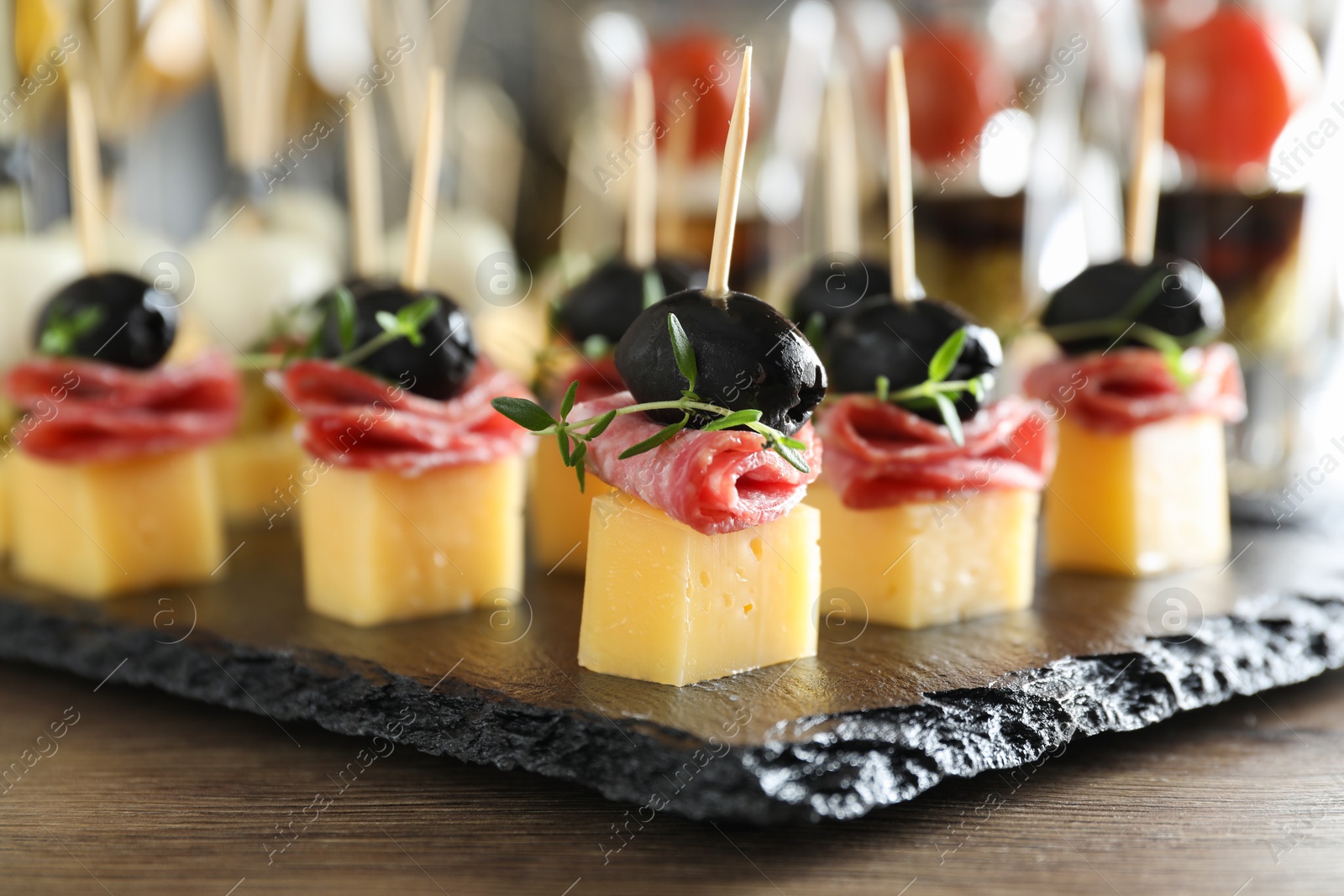 Photo of Tasty canapes with cheese, black olives and salami on wooden table, closeup