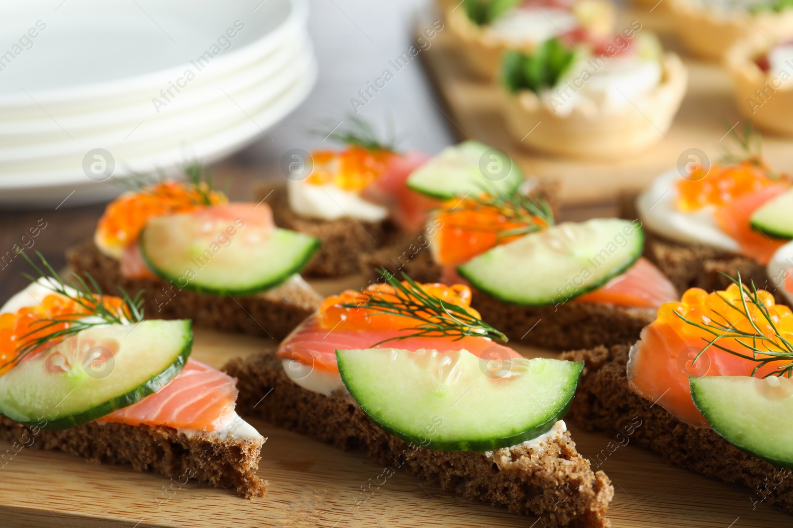 Photo of Tasty canapes with salmon and cucumber on wooden table, closeup