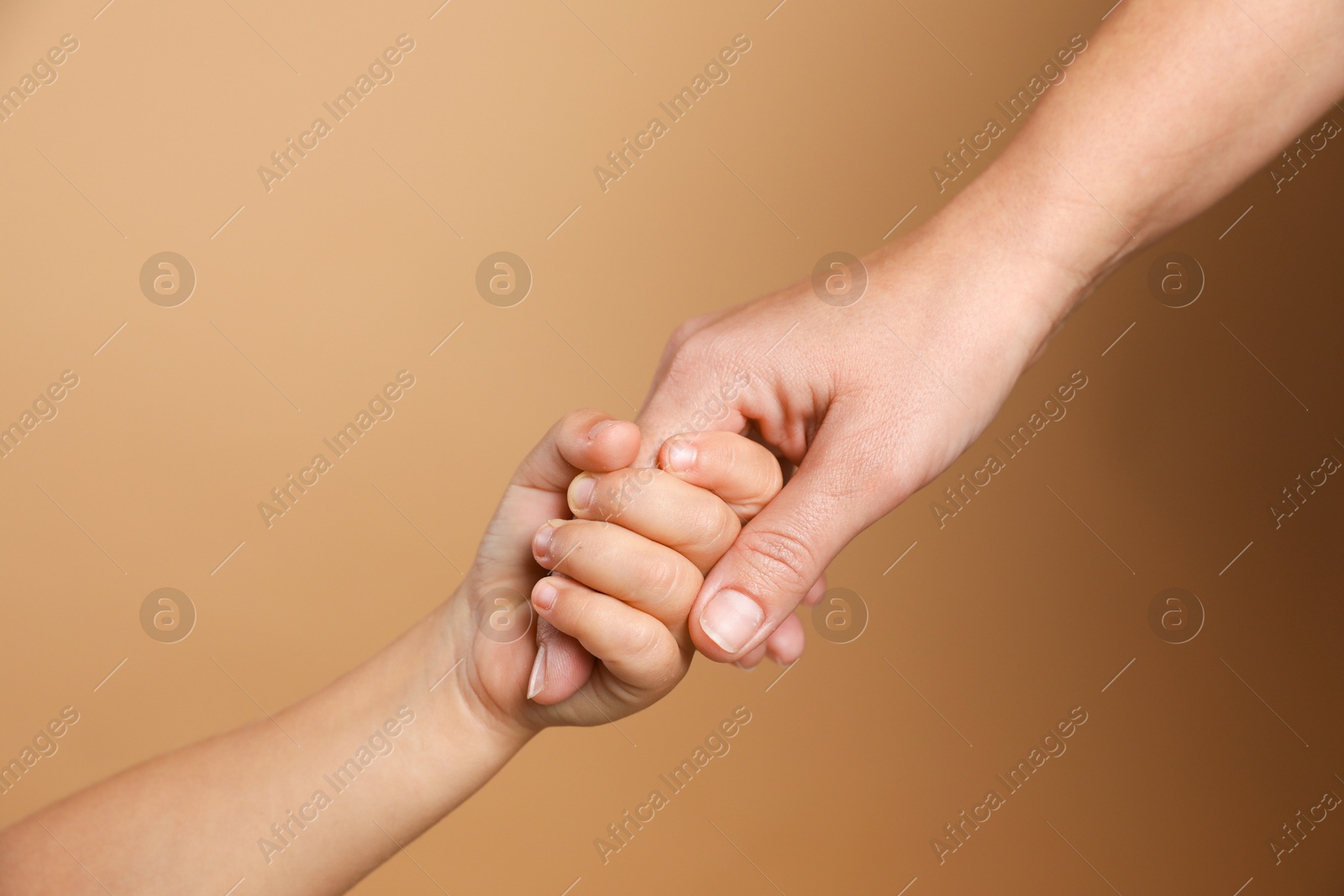 Photo of Mother and child holding hands on beige background, closeup