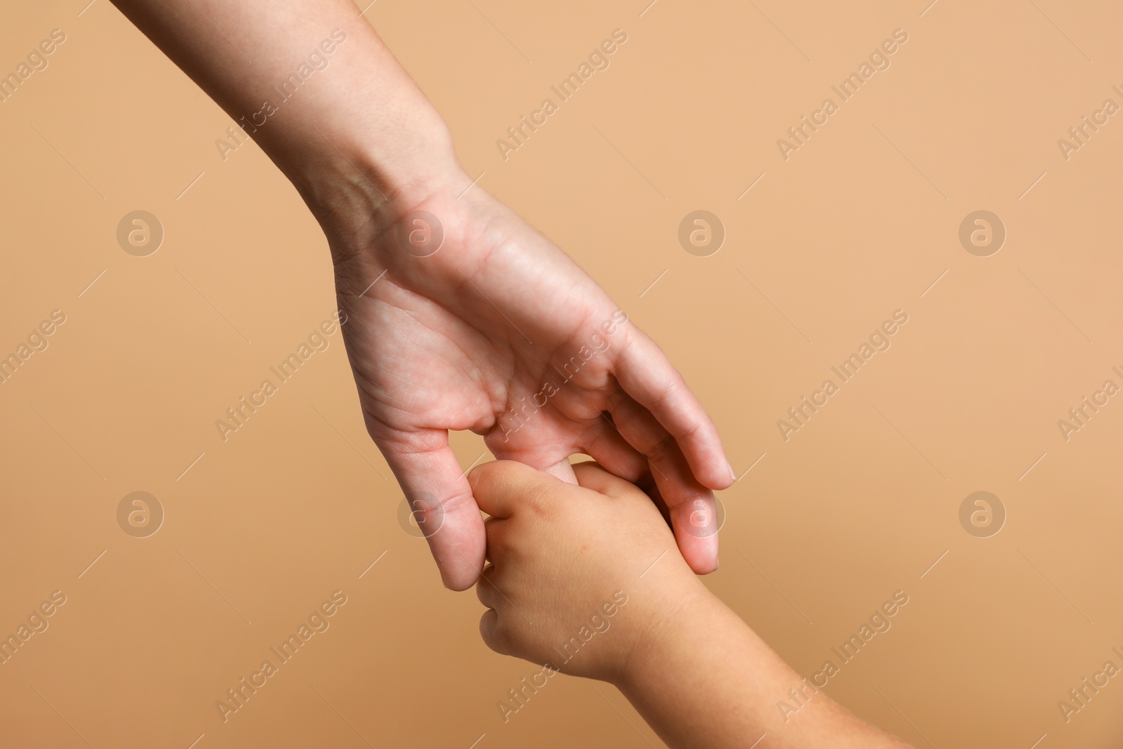 Photo of Mother and child holding hands on beige background, closeup