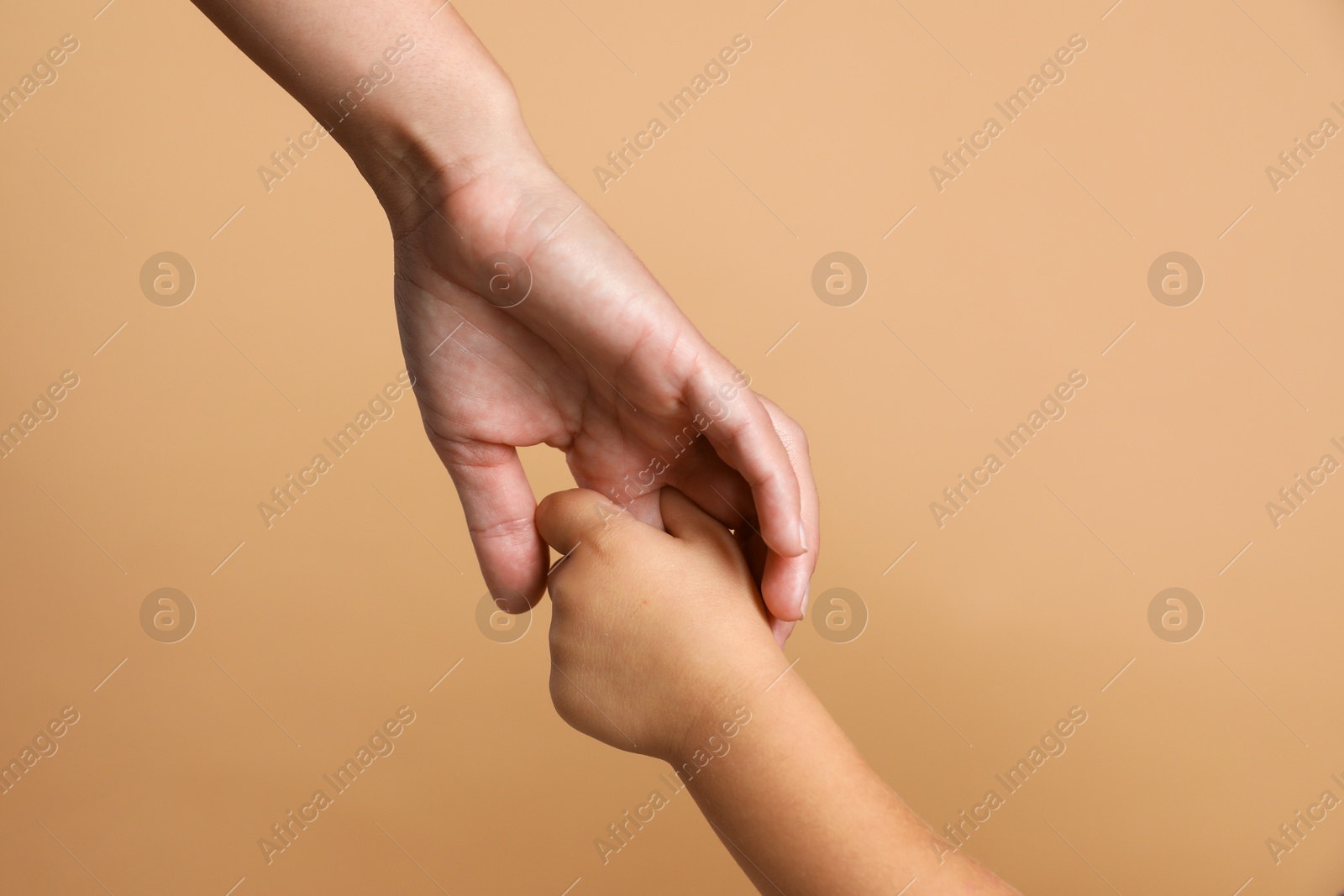 Photo of Mother and child holding hands on beige background, closeup