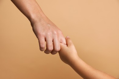 Photo of Mother and child holding hands on beige background, closeup