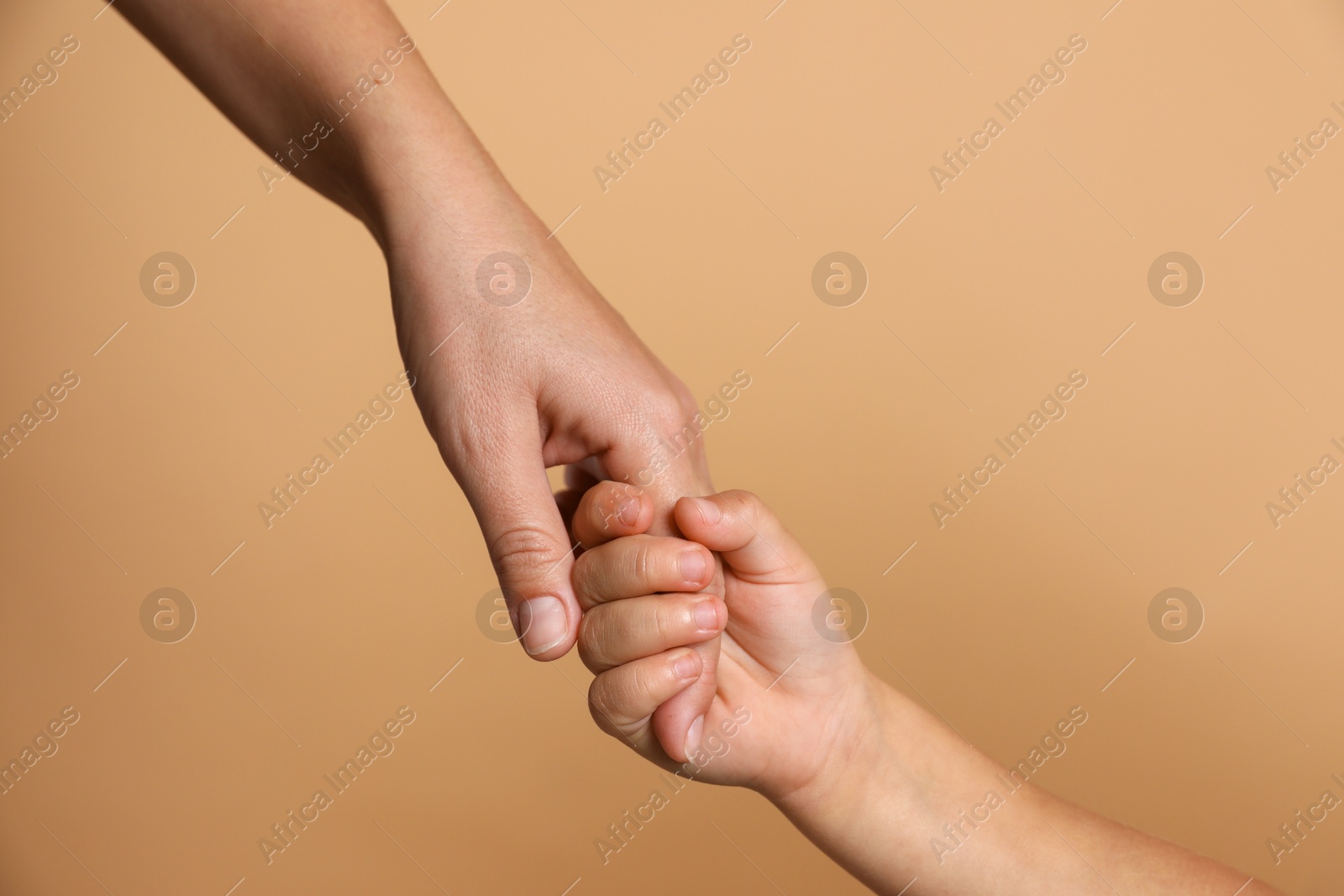 Photo of Mother and child holding hands on beige background, closeup