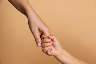 Photo of Mother and child holding hands on beige background, closeup