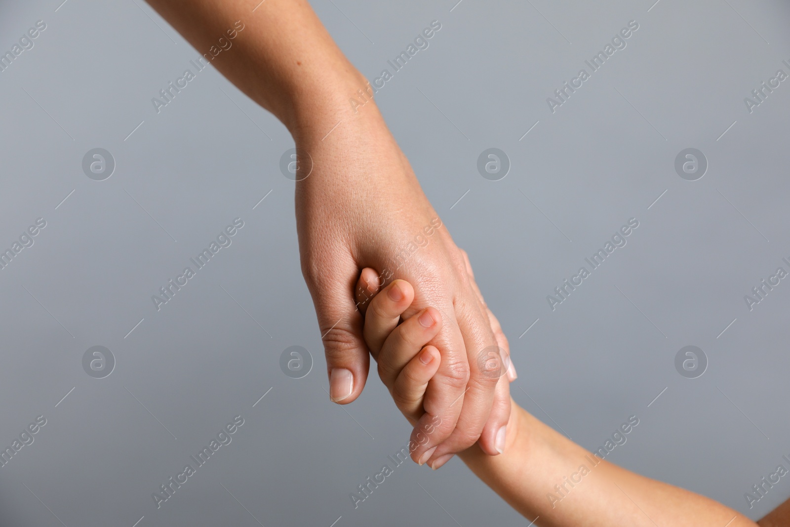 Photo of Mother and child holding hands on grey background, closeup